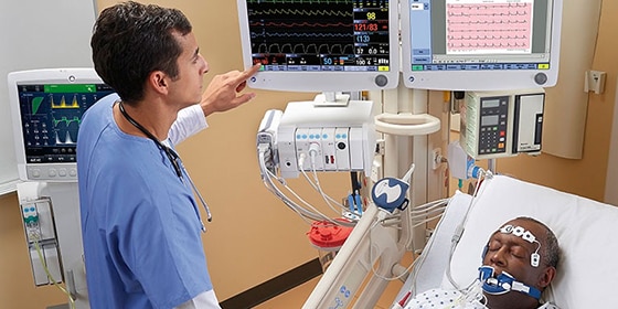 İki hasta bakıcı hasta verilerini ekranda gösteren GE Healthcare CARESCAPE B850 monitörün bulunduğu bir hastane odasındaki kuvözün yanında konuşuyor.