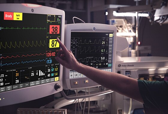 A caregivers is touching at the display screen of a GE Healthcare CARESCAPE B850 patient monitor to learn patient data.