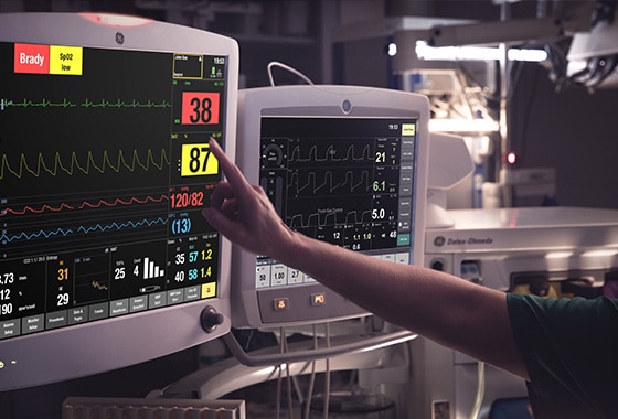 A caregivers is touching at the display screen of a GE Healthcare CARESCAPE B850 patient monitor to learn patient data.