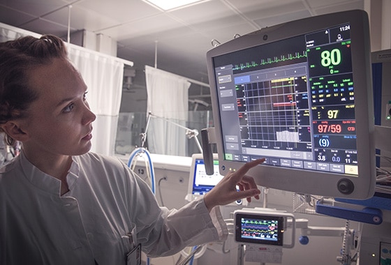 A caregivers is touching at the display screen of a GE Healthcare CARESCAPE B850 patient monitor to learn patient data.